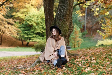Téléchargez les photos : Femme aux cheveux bruns dans un chapeau noir et poncho dans le parc - en image libre de droit