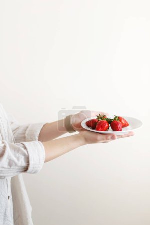 Photo for Woman cook holds a plate with red fresh strawberries in her hands - Royalty Free Image