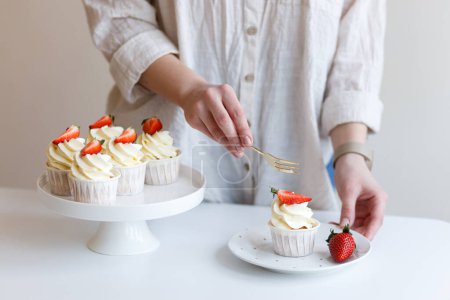 Foto de Joven mujer cocinero gustos crema cupcake con fresas frescas - Imagen libre de derechos