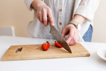 Téléchargez les photos : Femelle cuisinière coupe des fraises rouges fraîches avec couteau dans la cuisine - en image libre de droit