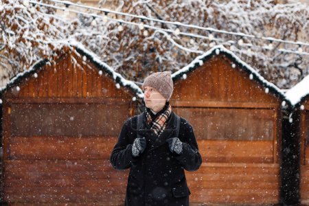 Téléchargez les photos : Homme en manteau au milieu d'une ville enneigée pendant les vacances - en image libre de droit