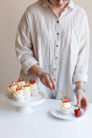 Foto de Joven mujer cocinero gustos crema cupcake con fresas frescas - Imagen libre de derechos