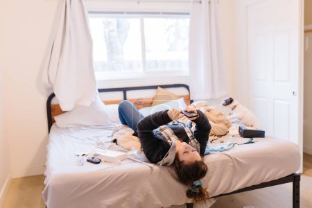 Téléchargez les photos : Femme adulte allongée sur un lit désordonné regardant le téléphone - en image libre de droit
