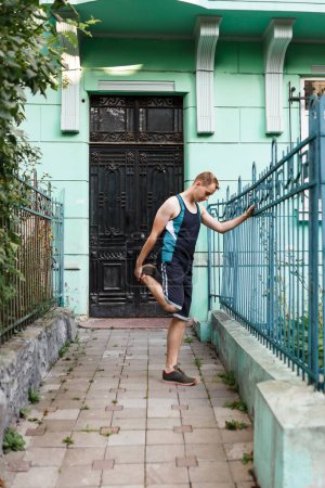 Téléchargez les photos : Jeune homme s'étire avant de faire du jogging près de chez lui seul en été - en image libre de droit