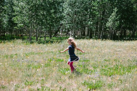 Foto de Niña jugando en un prado de flores con bosque en verano - Imagen libre de derechos