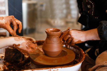 Photo for Potter with a student on the potter's wheel makes dishes from clay - Royalty Free Image