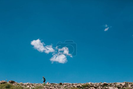 Foto de Niño caminando en la caminata en la colina rocosa con el cielo azul en el sol - Imagen libre de derechos
