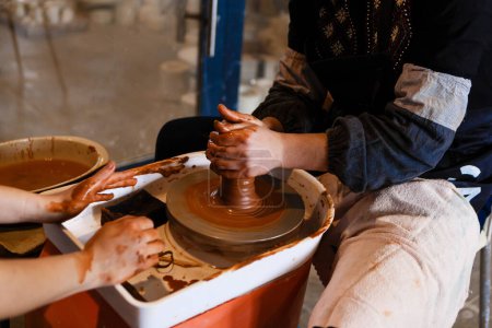 Photo for Potter with student on potter's wheel makes dishes from clay - Royalty Free Image