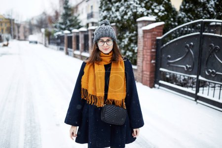 Téléchargez les photos : Femme en écharpe jaune et manteau bleu au milieu de la rue enneigée - en image libre de droit
