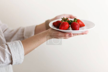 Foto de Mujer cocinera sostiene un plato con fresas frescas rojas en sus manos - Imagen libre de derechos