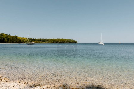 Foto de Veleros serenos a la deriva por una costa tranquila y guijarros. - Imagen libre de derechos