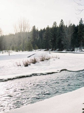 Teilweise zugefrorener Fluss schneidet sich durch verschneite Landschaft in Montana