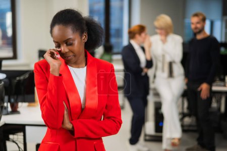 Téléchargez les photos : Une jeune femme africaine pleure à cause du ridicule de ses collègues. Discrimination raciale au bureau - en image libre de droit