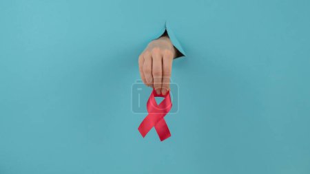 Photo for A womans hand with a red bow sticks out of a hole in a blue background. Breast cancer symbol - Royalty Free Image
