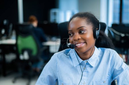 Foto de Mujer joven africana hablando con un cliente con auriculares. Empleada del call center - Imagen libre de derechos