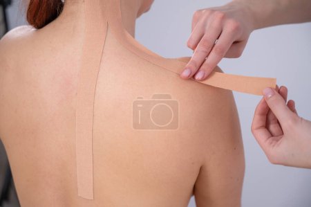 Foto de Médico femenino pega cintas kinesio en el hombro de los pacientes - Imagen libre de derechos