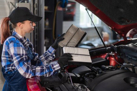 Photo for Caucasian female auto mechanic changes the engine air filter in the car - Royalty Free Image