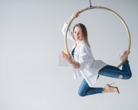 Photo for Caucasian female gymnast doing aerial hoop exercises and using smartphone - Royalty Free Image