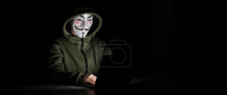 Photo for June 5, 2022 Novosibirsk, Russia: Anonymous in a hood is typing on a laptop in the dark - Royalty Free Image
