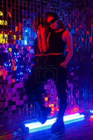 Portrait of a caucasian woman in sunglasses in neon light against a mirror wall
