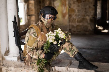 Photo for Caucasian woman in military uniform holding a machine gun and a bouquet of white roses - Royalty Free Image