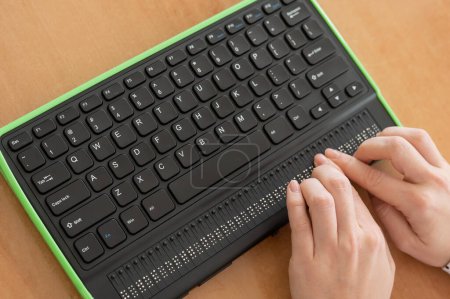 Foto de Una mujer ciega usa una computadora con una pantalla Braille y un teclado de computadora. Dispositivo inclusivo - Imagen libre de derechos