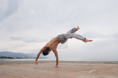 Photo for Shirtless caucasian man doing backflip on pebble beach - Royalty Free Image