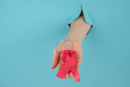 Photo for A womans hand with a red bow sticks out of a hole in a blue background. Breast cancer symbol - Royalty Free Image