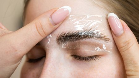Photo for The master uses a plastic film during lamination of the eyebrows - Royalty Free Image