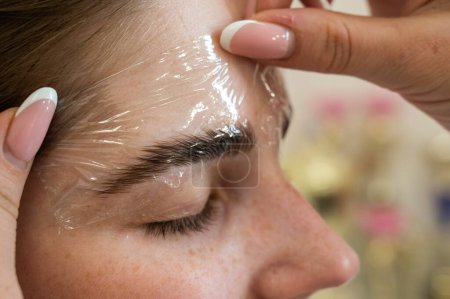 Photo for The master uses a plastic film during lamination of the eyebrows - Royalty Free Image