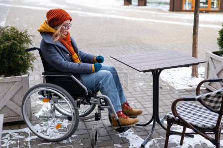 Foto de Mujer caucásica en silla de ruedas sentada en la mesa de café al aire libre - Imagen libre de derechos