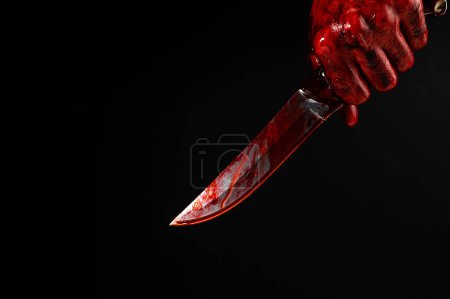 Téléchargez les photos : Un homme aux mains sanglantes brandit un couteau sur un fond noir - en image libre de droit