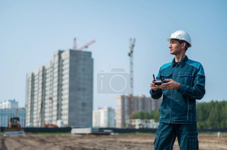 Foto de Un hombre con casco y mono controla un dron en un sitio de construcción. El constructor realiza la supervisión técnica - Imagen libre de derechos
