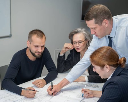 Photo for The boss gives instructions to three employees in the office conference room. Brainstorming engineers and architects - Royalty Free Image