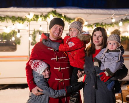 Téléchargez les photos : Heureuse grande famille célèbre Noël dans la nature et détient des étincelles. Les parents avec trois fils voyagent dans une maison mobile - en image libre de droit