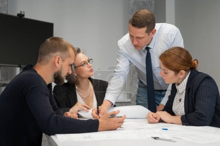 Photo for The boss gives instructions to three employees in the office conference room. Brainstorming engineers and architects - Royalty Free Image