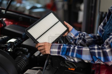 Photo for Caucasian female auto mechanic changes the engine air filter in the car - Royalty Free Image