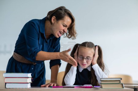Photo for A female teacher yells at a student. Little girl covers her ears with her hands - Royalty Free Image