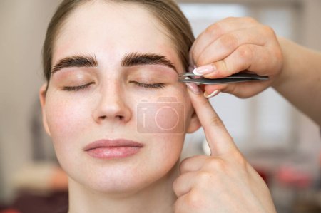 Photo for The master makes the client eyebrow correction with tweezers - Royalty Free Image