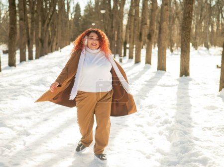 Téléchargez les photos : Une grosse femme écoute de la musique avec des écouteurs et danse dans le parc en hiver - en image libre de droit