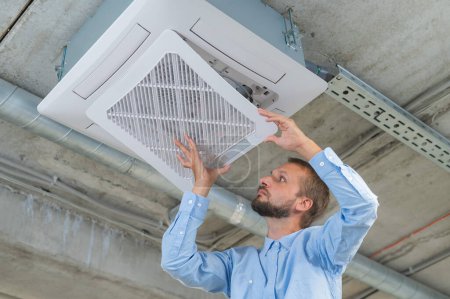 Kaukasischer bärtiger Mann repariert die Klimaanlage im Büro