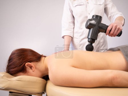 Téléchargez les photos : Médecin massant le dos d'une patiente avec un pistolet masseur à percussion - en image libre de droit