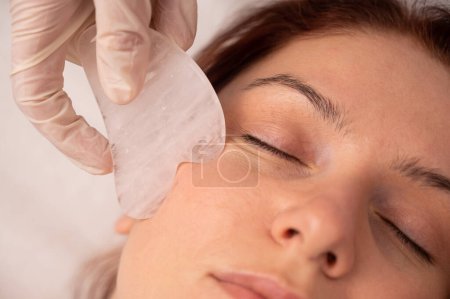 Foto de A cosmetologist uses a gouache scraper on a clients face - Imagen libre de derechos