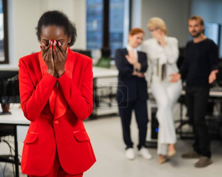 Foto de Una joven africana llorando por el ridículo de sus colegas. Discriminación racial en la oficina - Imagen libre de derechos
