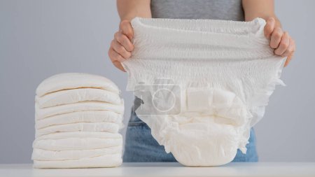 Téléchargez les photos : A woman chooses an adult diaper from a pile. Urinary incontinence problem - en image libre de droit