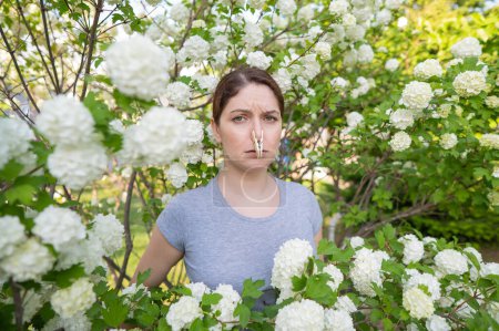 Téléchargez les photos : Unhappy woman with a clothespin on her nose on a walk in a blooming park - en image libre de droit
