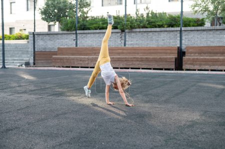 Téléchargez les photos : Fille caucasienne fait une roue sur le terrain de sport en plein air - en image libre de droit