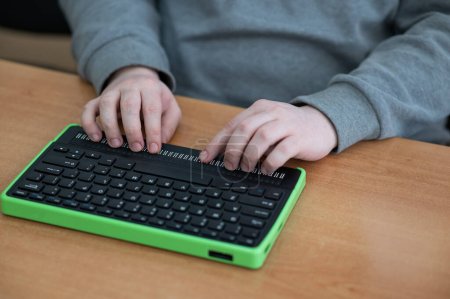 Foto de Un ciego usa una computadora con una pantalla Braille y un teclado de computadora. Dispositivo inclusivo - Imagen libre de derechos
