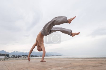 Photo for Shirtless caucasian man doing backflip on pebble beach - Royalty Free Image