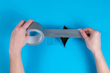 Woman sticking silver tape on a hole on a blue background